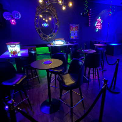 Neon-lit bar interior with tables and chairs under a blue-purple hue