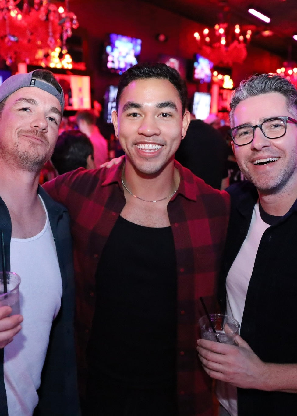 Three men posing together in a bar setting with drinks.