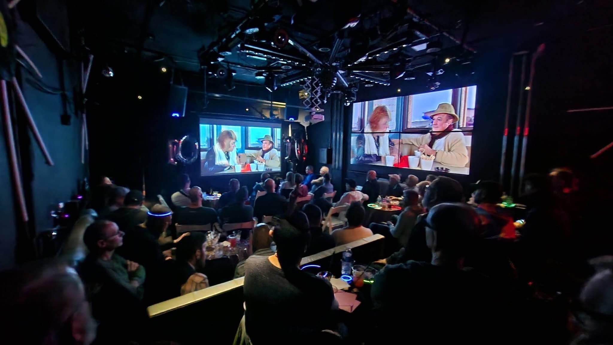 People watching a sports event on multiple screens in a dimly lit room.