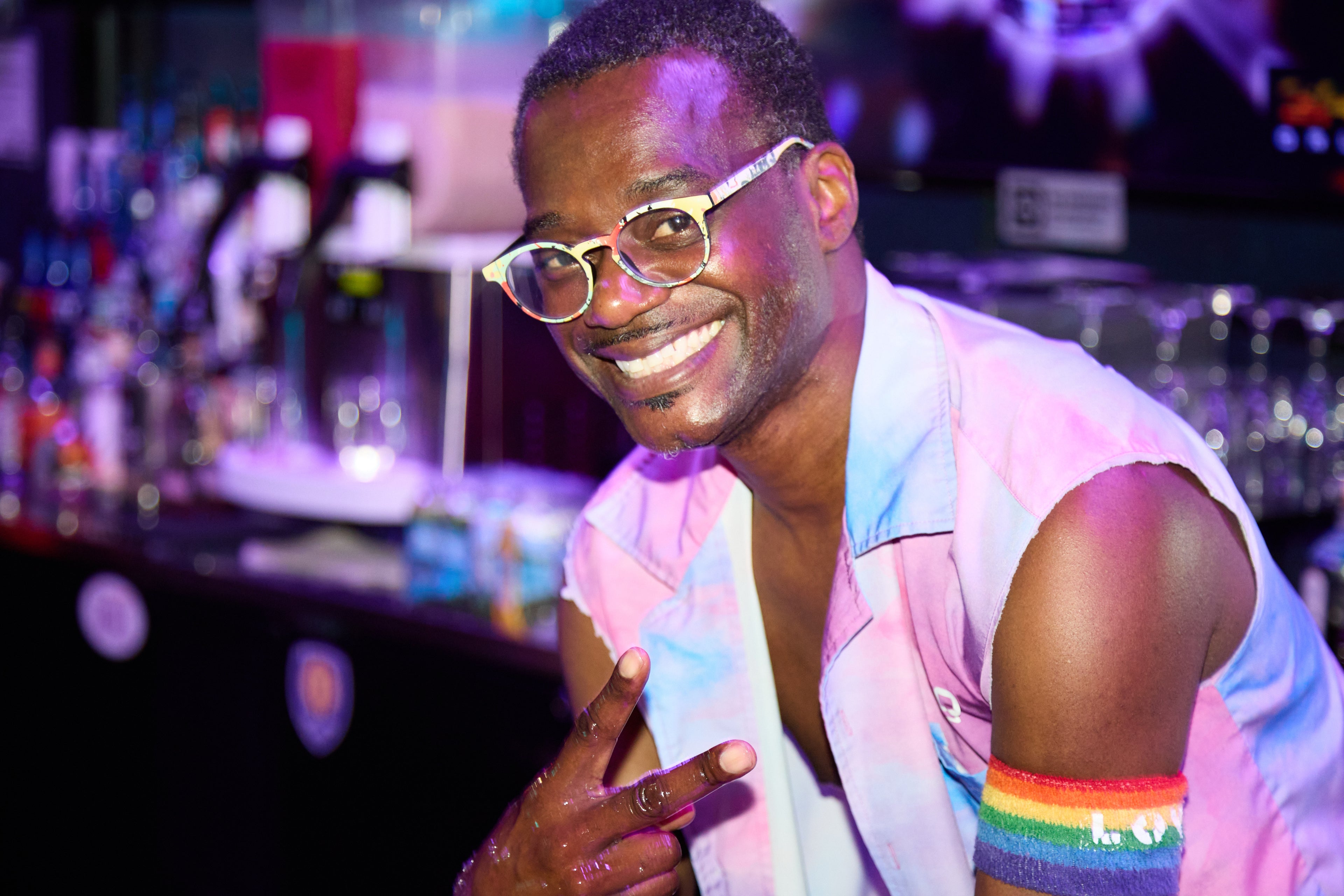 Person in a colorful outfit with rainbow wristband in a bar setting