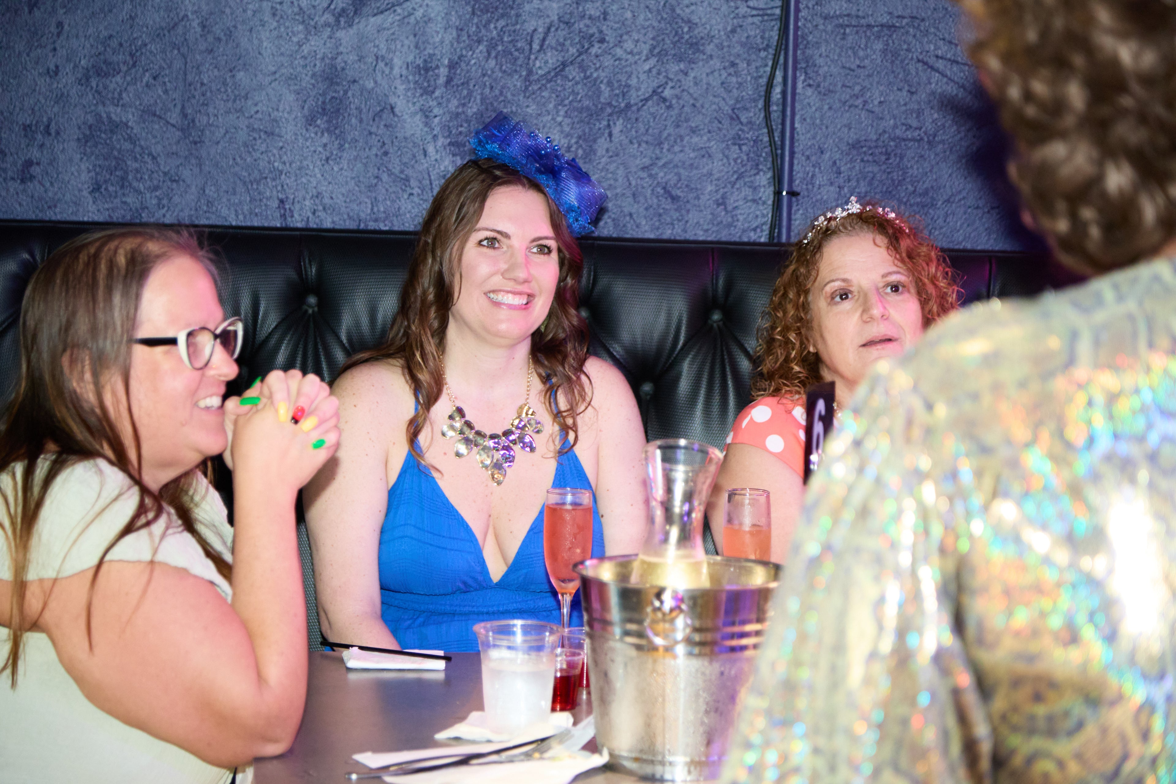 Three women sitting at a table with drinks and a colorful background