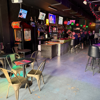 Bar interior with seating area, arcade games, and television screens.