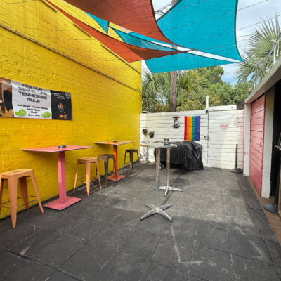 Outdoor seating area with colorful tables and chairs against a yellow wall.