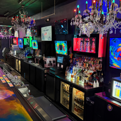 Bar with colorful lighting, televisions, and a variety of drinks.
