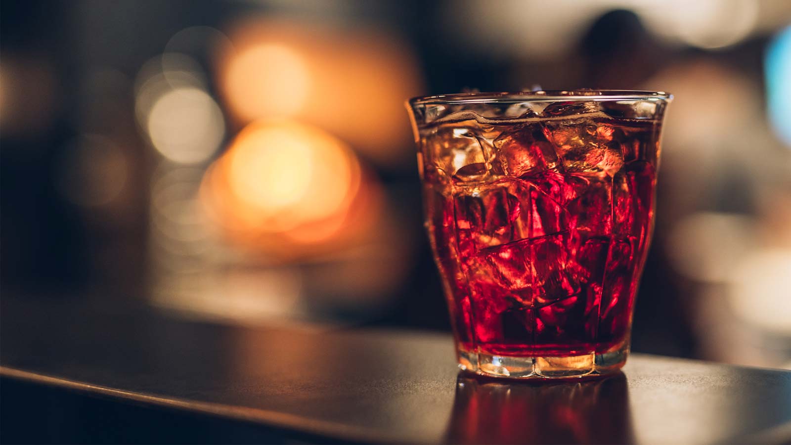 Glass of red cocktail with ice cubes on a bar counter with a blurred background