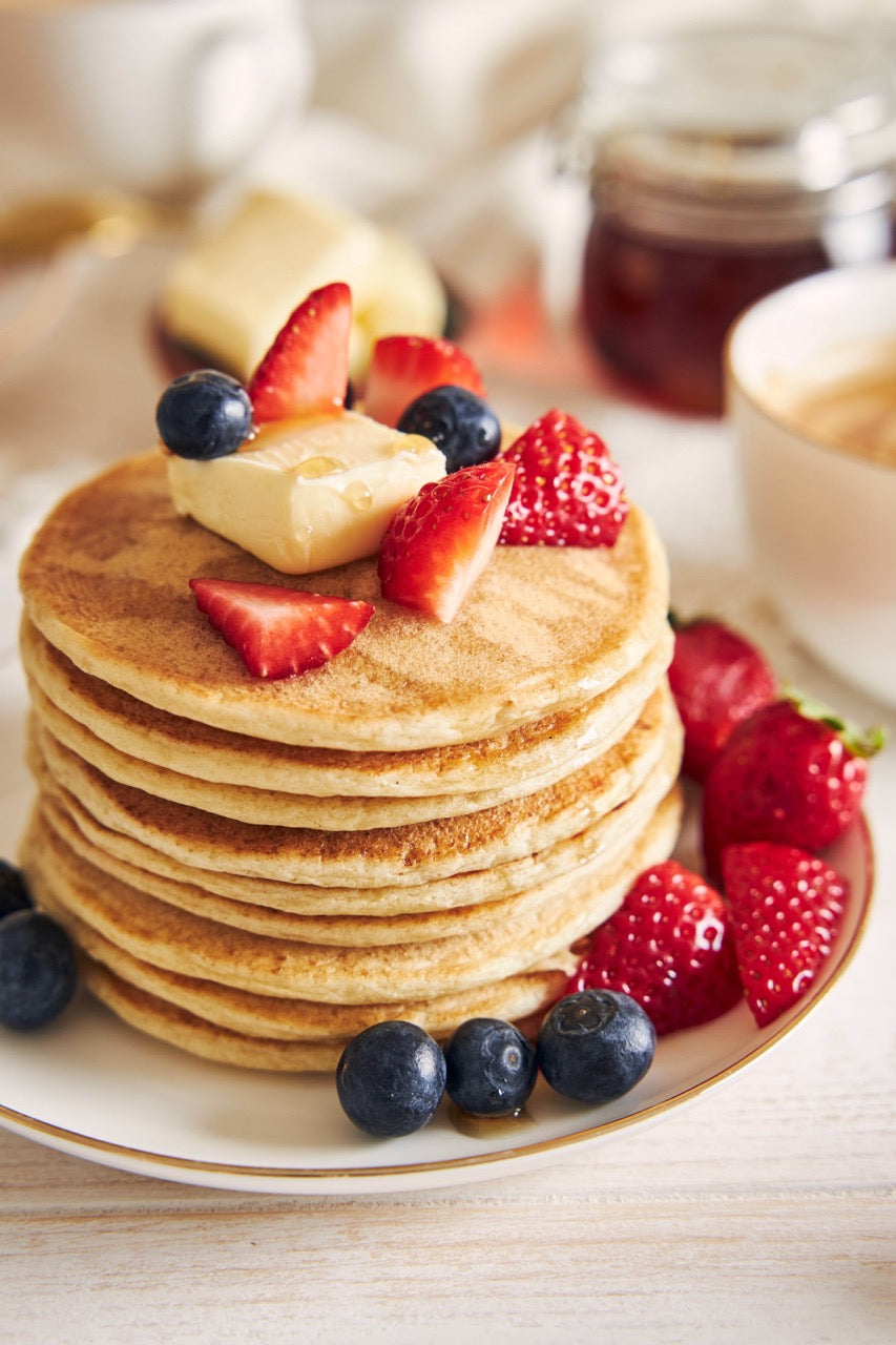 Stack of pancakes with berries and butter on a plate, with a blurred background
